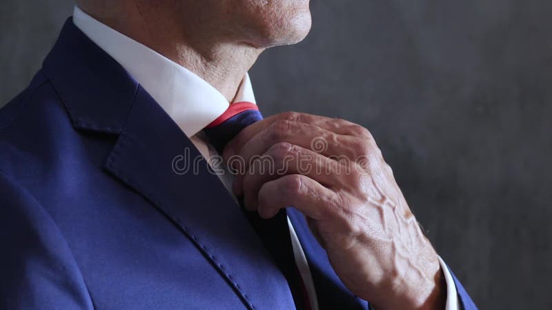 Men`s arms adjust blue necktie on throat against gray wall, side view