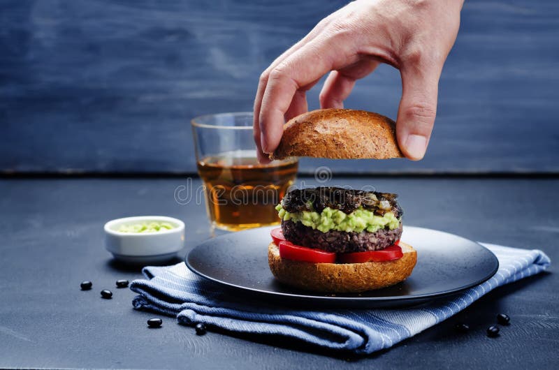 Men s hands holding the black bean burger with mashed avocado, c