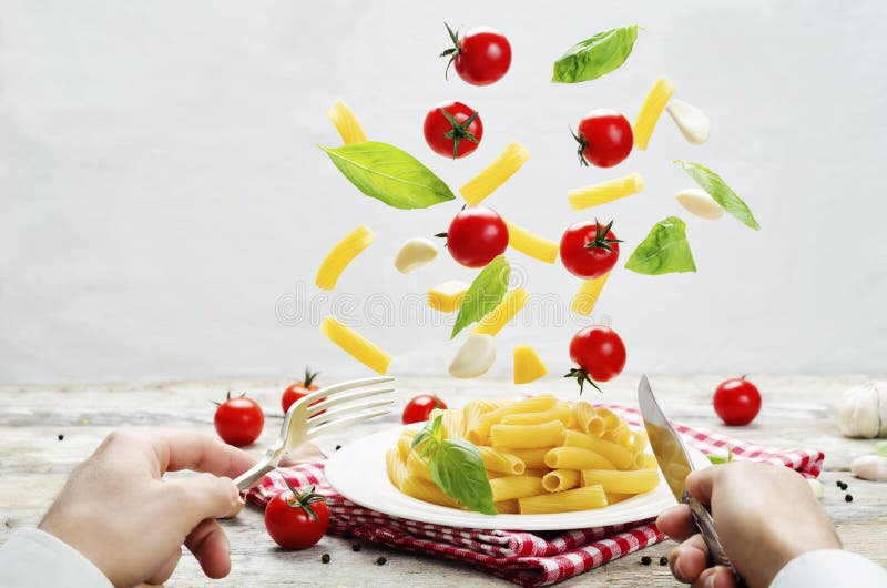 Men`s Hands with Knife and Fork and a Flying Pasta with Tomato a Stock