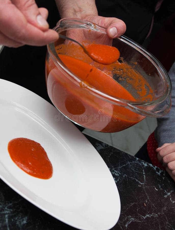 Men`s Hands Pouring Red Tomatoe or Chilly Sauce over Red Plate for Food Garnish. Ketchup Spill of Tomato sauce. Vertical