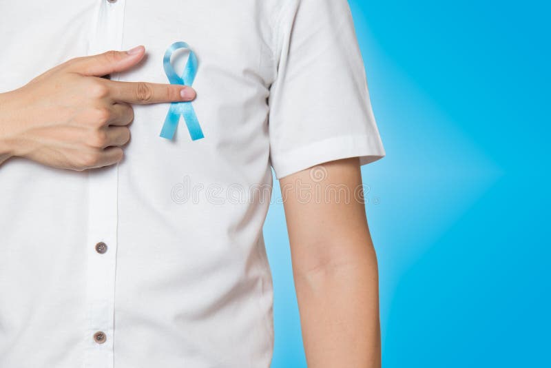 Men`s healthcare concept - close up of male hand pointing to light blue ribbon for prostate cancer at left chest on blue stock photography Men`s healthcare concept - close up of male hand pointing to light blue ribbon for prostate cancer at left chest on blue stock photography