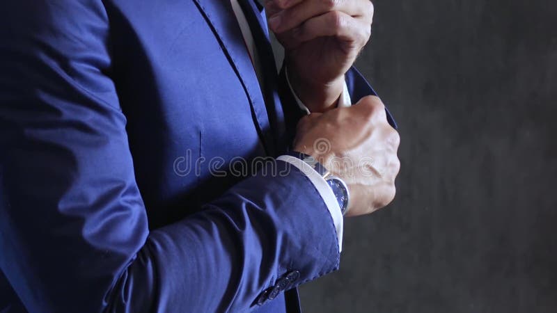 Men`s style, fiance fastens buttoning and cufflink on sleeves of shirt on background gray concrete wall