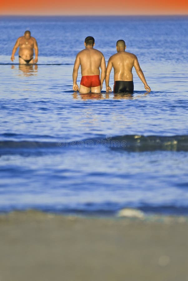 Three men wading in clear blue sea water at sunset. Three men wading in clear blue sea water at sunset.