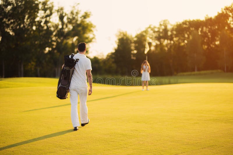 A man walks along the golf course with a golf club bag and heads towards the girl who is standing in front of him royalty free stock photo A man walks along the golf course with a golf club bag and heads towards the girl who is standing in front of him royalty free stock photo