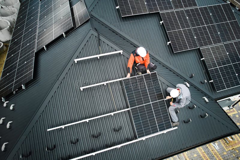 Men workers installing solar panels on roof of house.