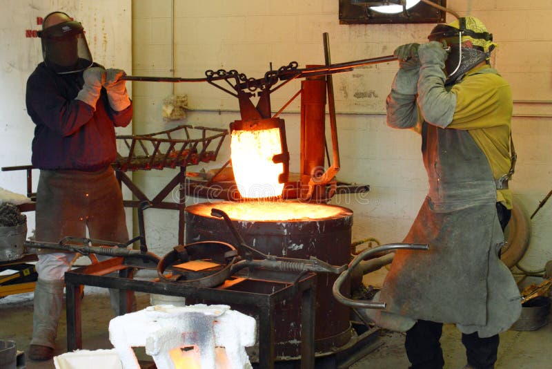 Dos hombres en negocios en fundición levantamiento un crisol de fusionado afuera de horno, agotador protector equipo.