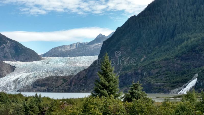 Mendenhall Glacier in Juneau Alaska. Large Glacier sliding into a lake with a waterfall beside it. Very popular tourist stop. Perfect Utopia on a calm lake a stock photo Mendenhall Glacier in Juneau Alaska. Large Glacier sliding into a lake with a waterfall beside it. Very popular tourist stop. Perfect Utopia on a calm lake a stock photo