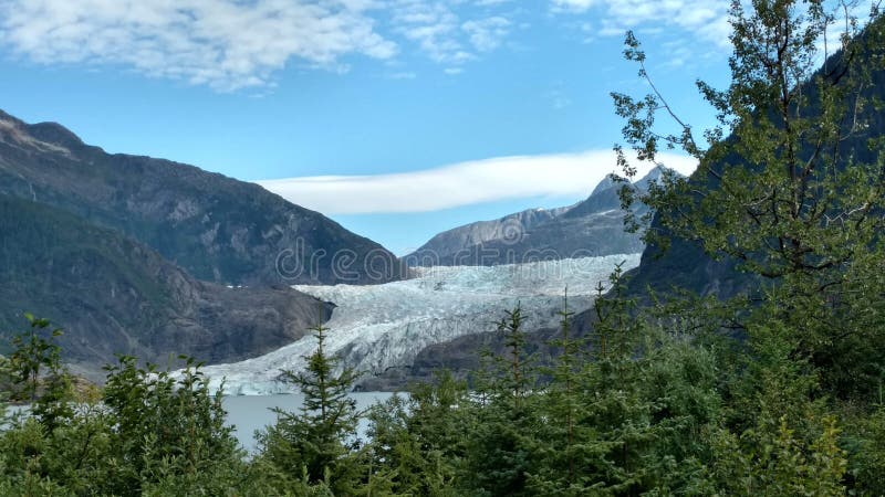 Mendenhall Glacier in Juneau Alaska. Large Glacier sliding into a lake with a waterfall beside it. Very popular tourist stop. Perfect Utopia on a calm lake a stock image Mendenhall Glacier in Juneau Alaska. Large Glacier sliding into a lake with a waterfall beside it. Very popular tourist stop. Perfect Utopia on a calm lake a stock image