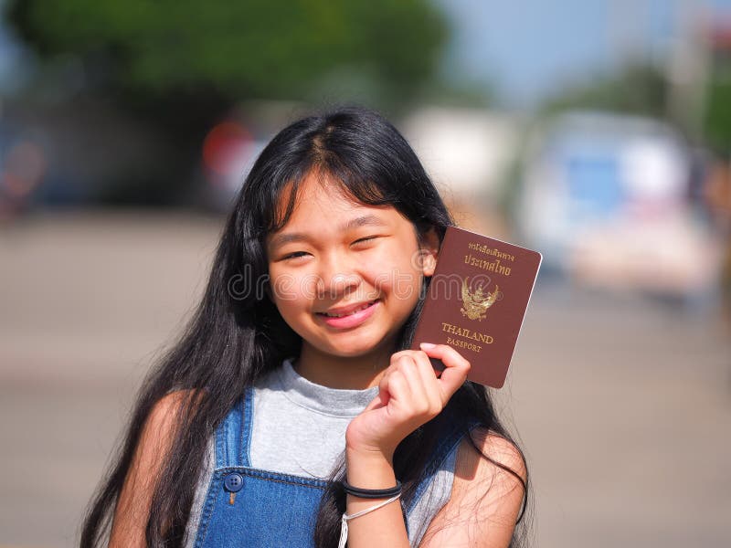 Menina adolescente asiática com o cabelo preto longo que guarda o passaporte tailandês fotografia de stock Menina adolescente asiática com o cabelo preto longo que guarda o passaporte tailandês fotografia de stock