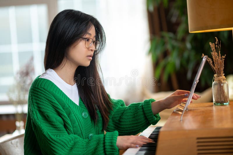 Menina adorável asiática examinando a folha de música e parecendo envolvida foto de stock