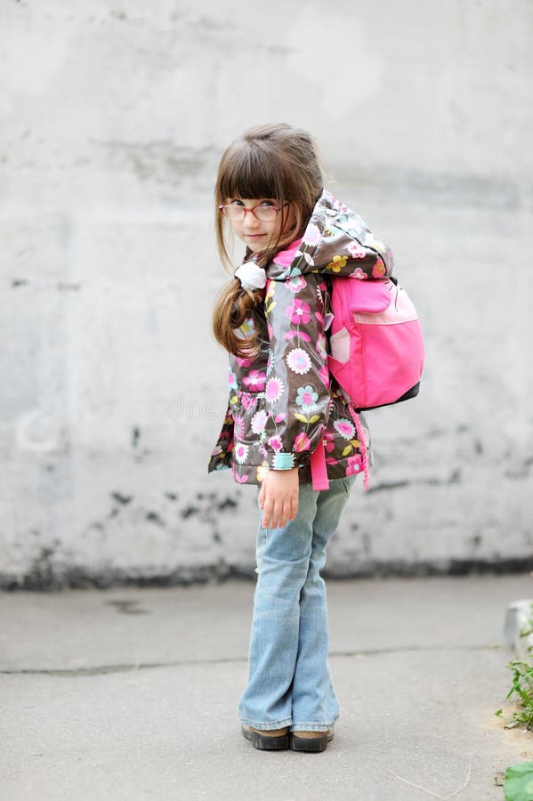 Adorable preschooler girl in glasses and colorful raincoat with pink back pack on the way to school. Adorable preschooler girl in glasses and colorful raincoat with pink back pack on the way to school