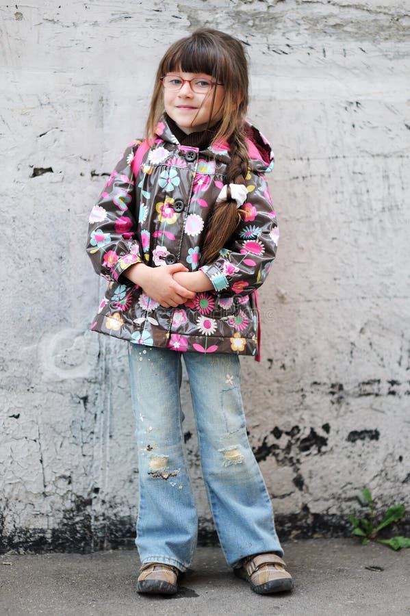 Adorable preschooler girl in glasses and colorful raincoat with pink back pack on the way to school. Adorable preschooler girl in glasses and colorful raincoat with pink back pack on the way to school