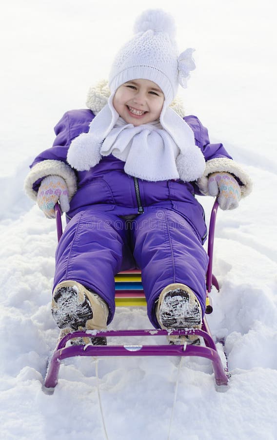 Menina adorável em um trenó no dia ensolarado do inverno foto de stock Menina adorável em um trenó no dia ensolarado do inverno foto de stock