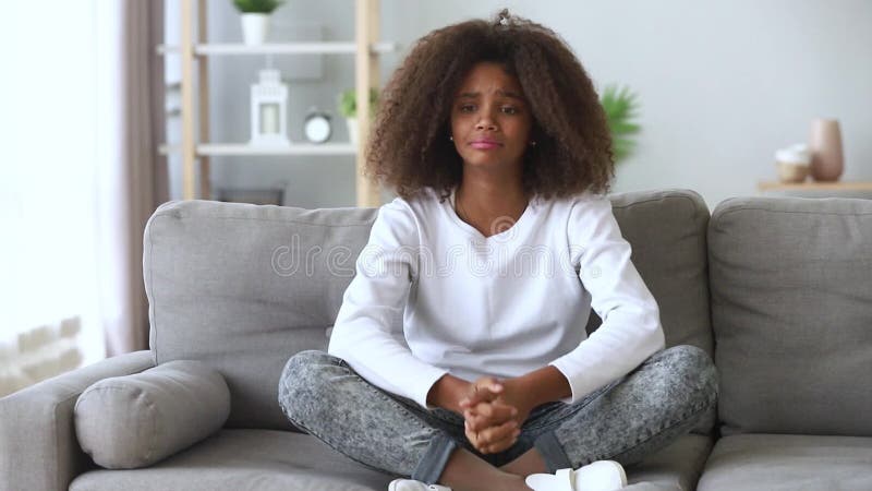Menina africana pré-adolescente sentada no sofá chorando não parece feliz
