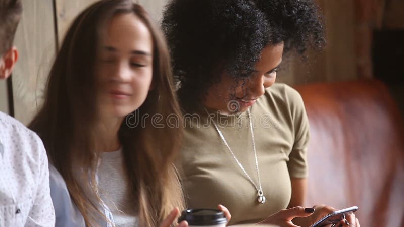 A menina afro-americano obcecou o smartphone usando na reunião com amigos multi-étnicos