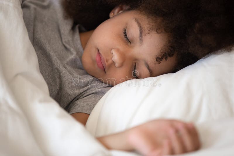 Menina afro-americano pequena bonito da criança que dorme apenas na cama