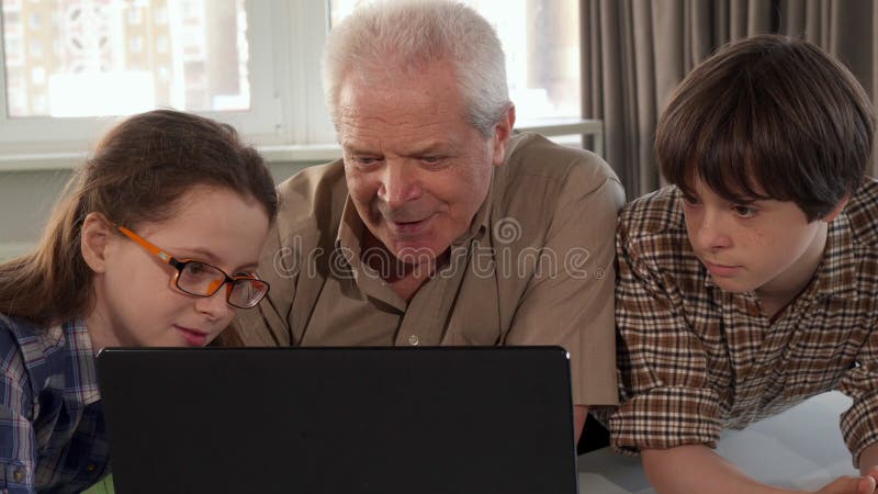 A menina ajuda seu vovô a datilografar no portátil imagens de stock royalty free
