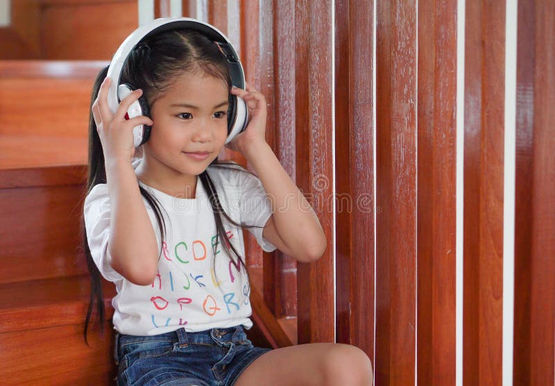 Menina asiática bonita ouvindo música com fones de ouvido nas escadas em casa foto de stock Menina asiática bonita ouvindo música com fones de ouvido nas escadas em casa foto de stock