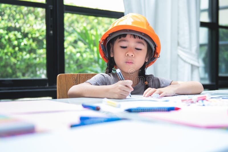 Menina asiática de 6 anos usando capacete de engenheiro está colorindo com intenção imagens de stock