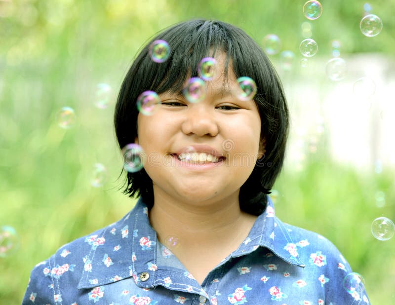 A menina asiática está sorrindo com bolhas de sabão ao redor imagem de stock A menina asiática está sorrindo com bolhas de sabão ao redor imagem de stock