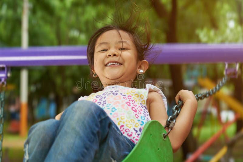 Menina asiática feliz em balanços imagem de stock royalty free Menina asiática feliz em balanços imagem de stock royalty free