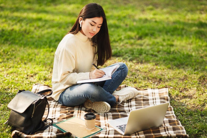 Menina asiática que faz trabalhos de casa, escrevendo notas e usando o portátil fotos de stock Menina asiática que faz trabalhos de casa, escrevendo notas e usando o portátil fotos de stock