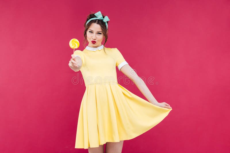 Menina atrativa de sorriso do pinup no vestido amarelo que mostra o pirulito doce fotos de stock Menina atrativa de sorriso do pinup no vestido amarelo que mostra o pirulito doce fotos de stock