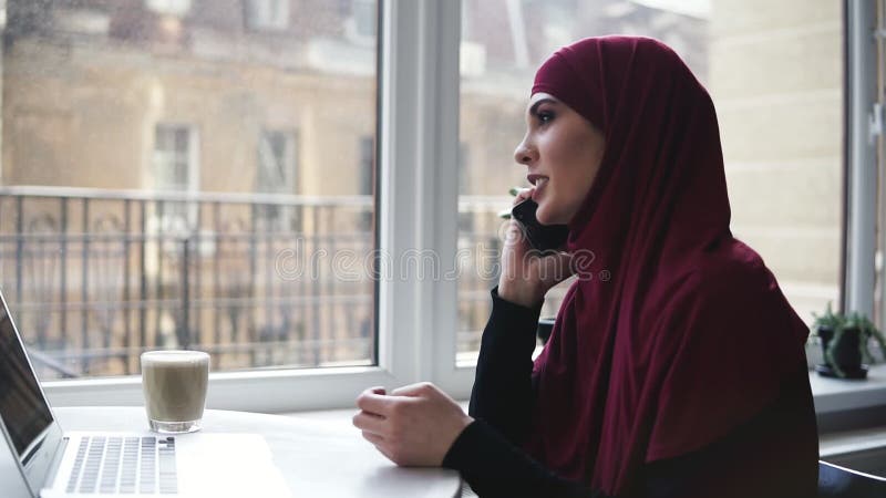 A menina atrativa nova da nacionalidade irreconhecível com hijab em sua cabeça falar a alguém no telefone quando ela