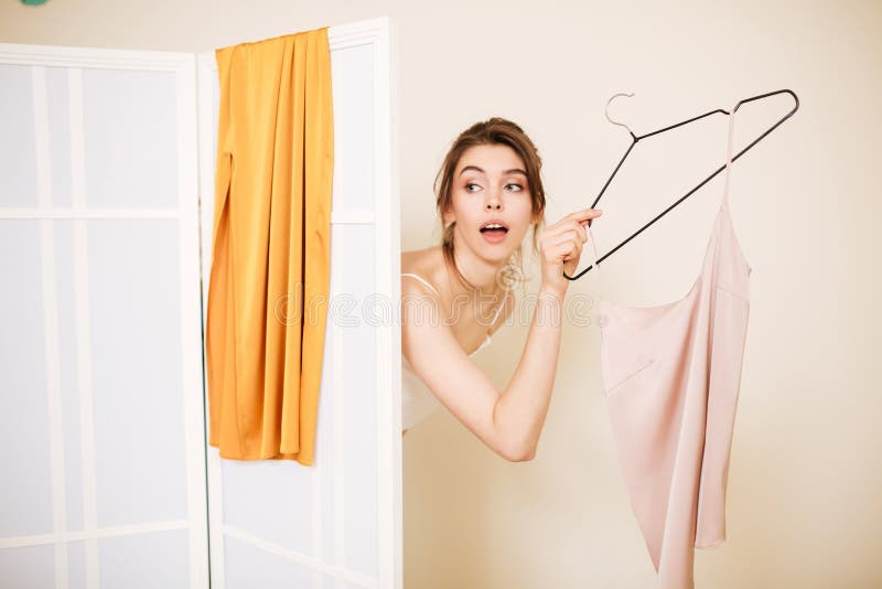 Menina bonita com o t-shirt no gancho que olha pensativamente fora da sala de encaixe na loja da roupa foto de stock Menina bonita com o t-shirt no gancho que olha pensativamente fora da sala de encaixe na loja da roupa foto de stock