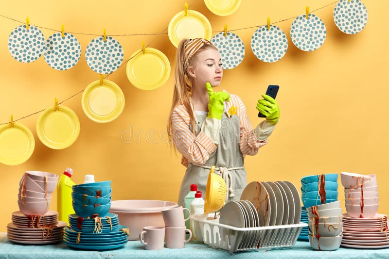 Menina bonita de encantamento nas luvas que guardam o telefone esperto ao fazer pratos fotos de stock Menina bonita de encantamento nas luvas que guardam o telefone esperto ao fazer pratos fotos de stock