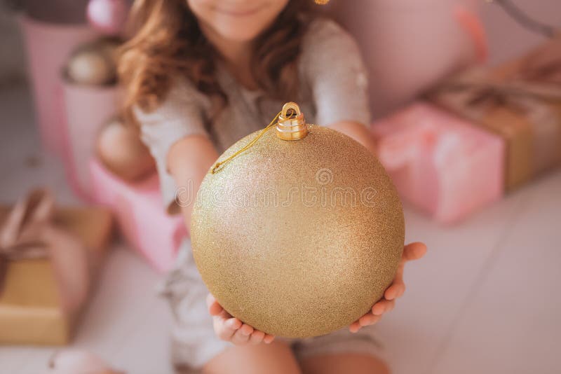 Menina bonita de sorriso que guarda a bola dourada enorme do feriado nas mãos foto de stock royalty free Menina bonita de sorriso que guarda a bola dourada enorme do feriado nas mãos foto de stock royalty free