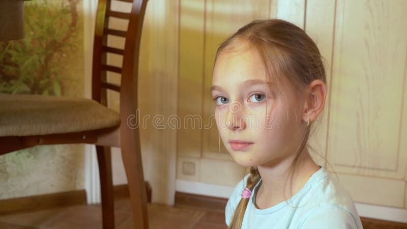 Menina bonita e séria sentada no chão e olhando para a câmera no interior