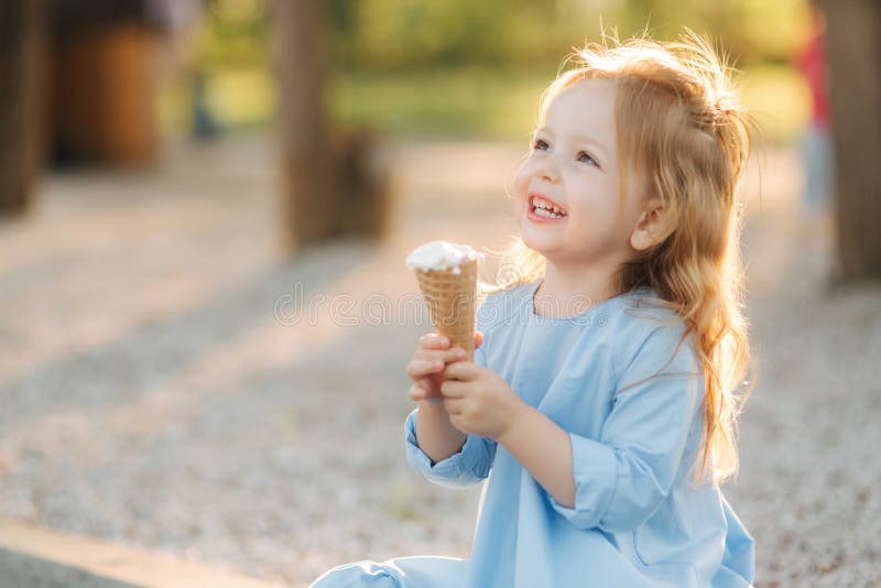 Menina bonita em um vestido azul que come um gelado imagem de stock Menina bonita em um vestido azul que come um gelado imagem de stock
