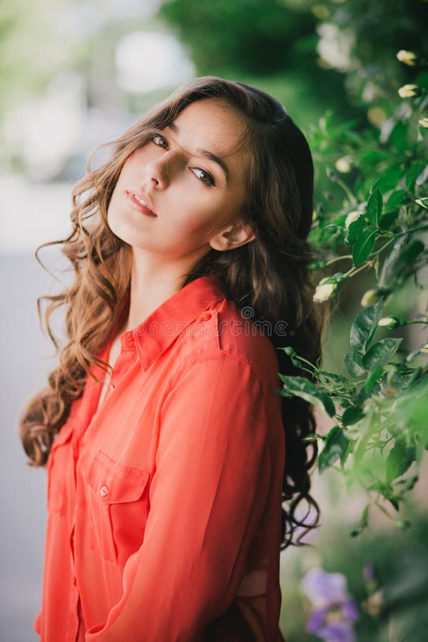 Menina bonita em uma camisa vermelha que levanta em uma rua imagem de stock Menina bonita em uma camisa vermelha que levanta em uma rua imagem de stock