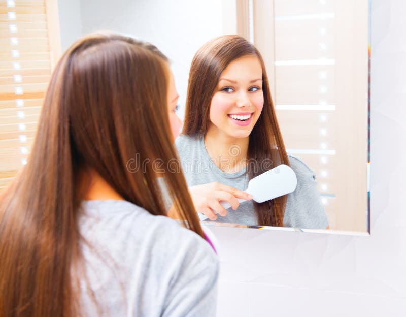 A menina bonita está penteando seu cabelo de seda longo imagens de stock A menina bonita está penteando seu cabelo de seda longo imagens de stock