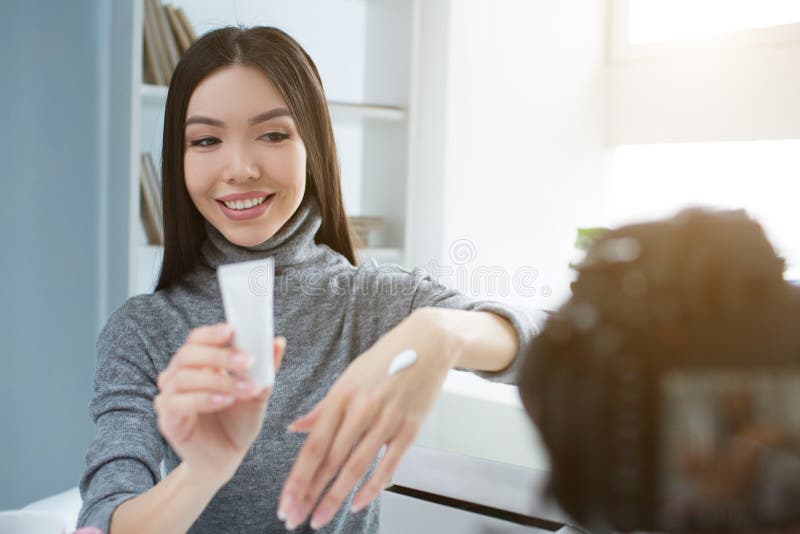 A menina bonita está sentando-se em uma sala perto da janela e está olhando-se à câmera Está sorrindo O blogger novo está mostran fotografia de stock royalty free A menina bonita está sentando-se em uma sala perto da janela e está olhando-se à câmera Está sorrindo O blogger novo está mostran fotografia de stock royalty free