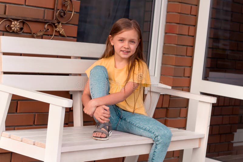 menina bonita feliz com o cabelo louro longo que veste a roupa ocasional que senta-se em um banco fotografia de stock menina bonita feliz com o cabelo louro longo que veste a roupa ocasional que senta-se em um banco fotografia de stock