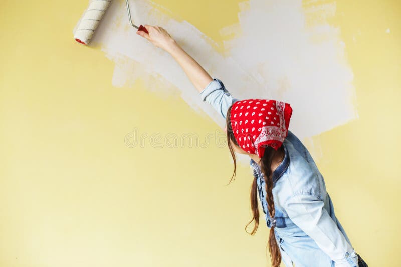 Menina bonita na faixa vermelha que pinta a parede com rolo da pintura imagem de stock Menina bonita na faixa vermelha que pinta a parede com rolo da pintura imagem de stock