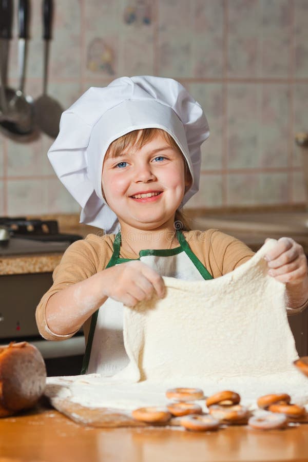 Menina bonita no chapéu de um cozinheiro chefe que cozinha o bolo doce