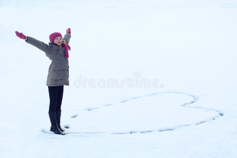 A menina bonita no inverno veste o coração de tiragem na neve Traço na neve fotos de stock royalty free A menina bonita no inverno veste o coração de tiragem na neve Traço na neve fotos de stock royalty free