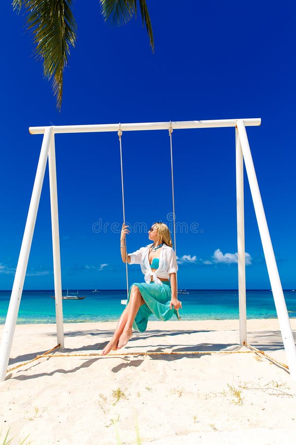 Menina bonita nova que senta-se em um balanço sob uma palmeira azul imagem de stock Menina bonita nova que senta-se em um balanço sob uma palmeira azul imagem de stock