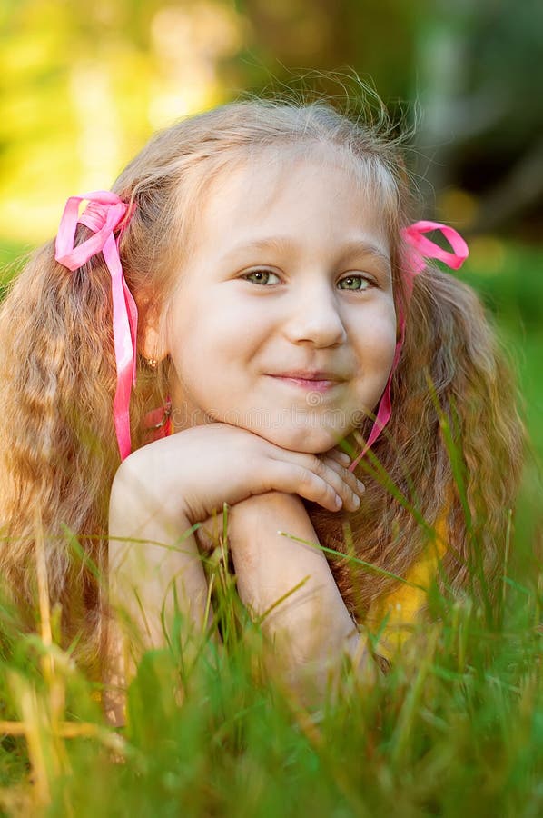A menina bonita pequena encontra-se na grama verde, verão do sol no pa da cidade fotografia de stock A menina bonita pequena encontra-se na grama verde, verão do sol no pa da cidade fotografia de stock