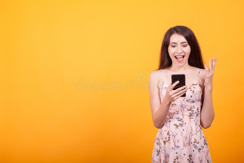 Menina bonita retirada feliz no vestido curto que guarda o telefone celular no estúdio sobre o fundo amarelo fotografia de stock Menina bonita retirada feliz no vestido curto que guarda o telefone celular no estúdio sobre o fundo amarelo fotografia de stock