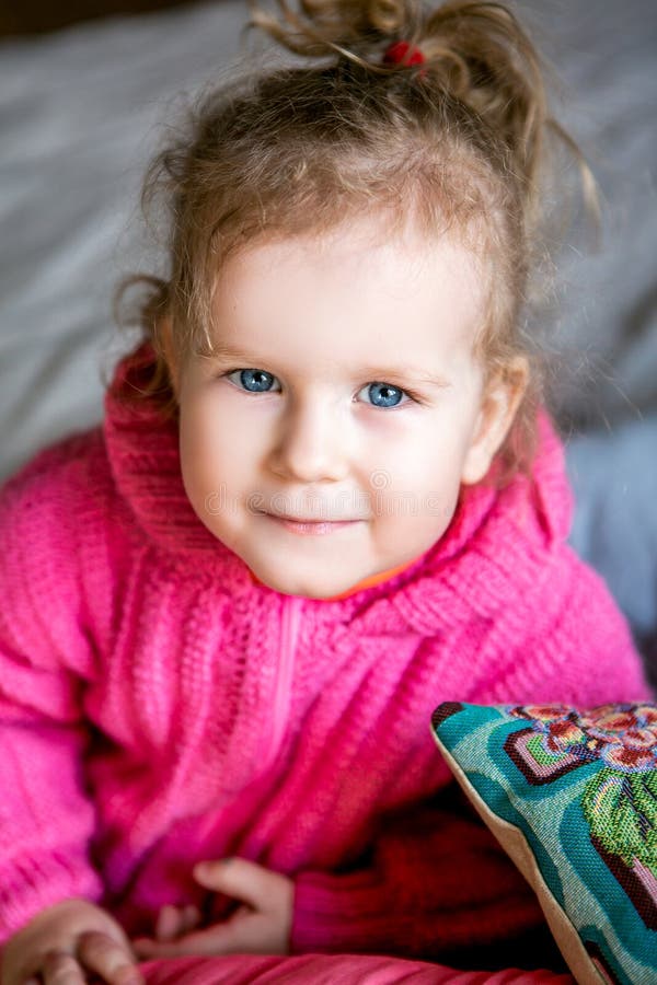 A menina bonito de olhos azuis em um revestimento cor-de-rosa olha na câmera fotos de stock royalty free A menina bonito de olhos azuis em um revestimento cor-de-rosa olha na câmera fotos de stock royalty free