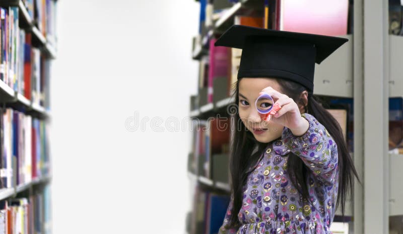 A menina bonito pequena com o papel do tampão e do diploma da graduação foto de stock A menina bonito pequena com o papel do tampão e do diploma da graduação foto de stock