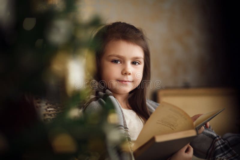 menina bonito pequena que senta-se perto da árvore de Natal e do livro de leitura fotos de stock menina bonito pequena que senta-se perto da árvore de Natal e do livro de leitura fotos de stock