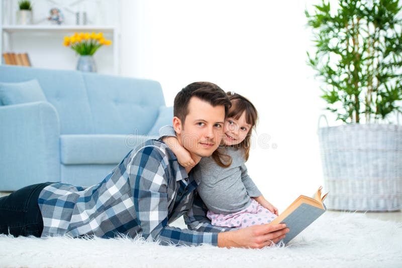Menina bonito que escuta o conto de fadas da leitura do paizinho que encontra-se no assoalho morno junto, importando-se o livro d fotografia de stock royalty free Menina bonito que escuta o conto de fadas da leitura do paizinho que encontra-se no assoalho morno junto, importando-se o livro d fotografia de stock royalty free