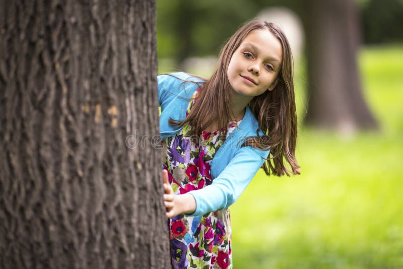 Menina bonito que espreita atrás de uma árvore Divertimento imagem de stock Menina bonito que espreita atrás de uma árvore Divertimento imagem de stock