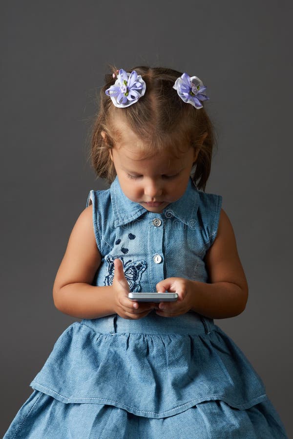 Menina bonito que usa o smartphone Fundo cinzento fotos de stock Menina bonito que usa o smartphone Fundo cinzento fotos de stock