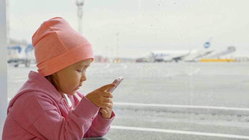 Menina bonito que usa o telefone esperto no aeroporto, close-up imagem de stock Menina bonito que usa o telefone esperto no aeroporto, close-up imagem de stock